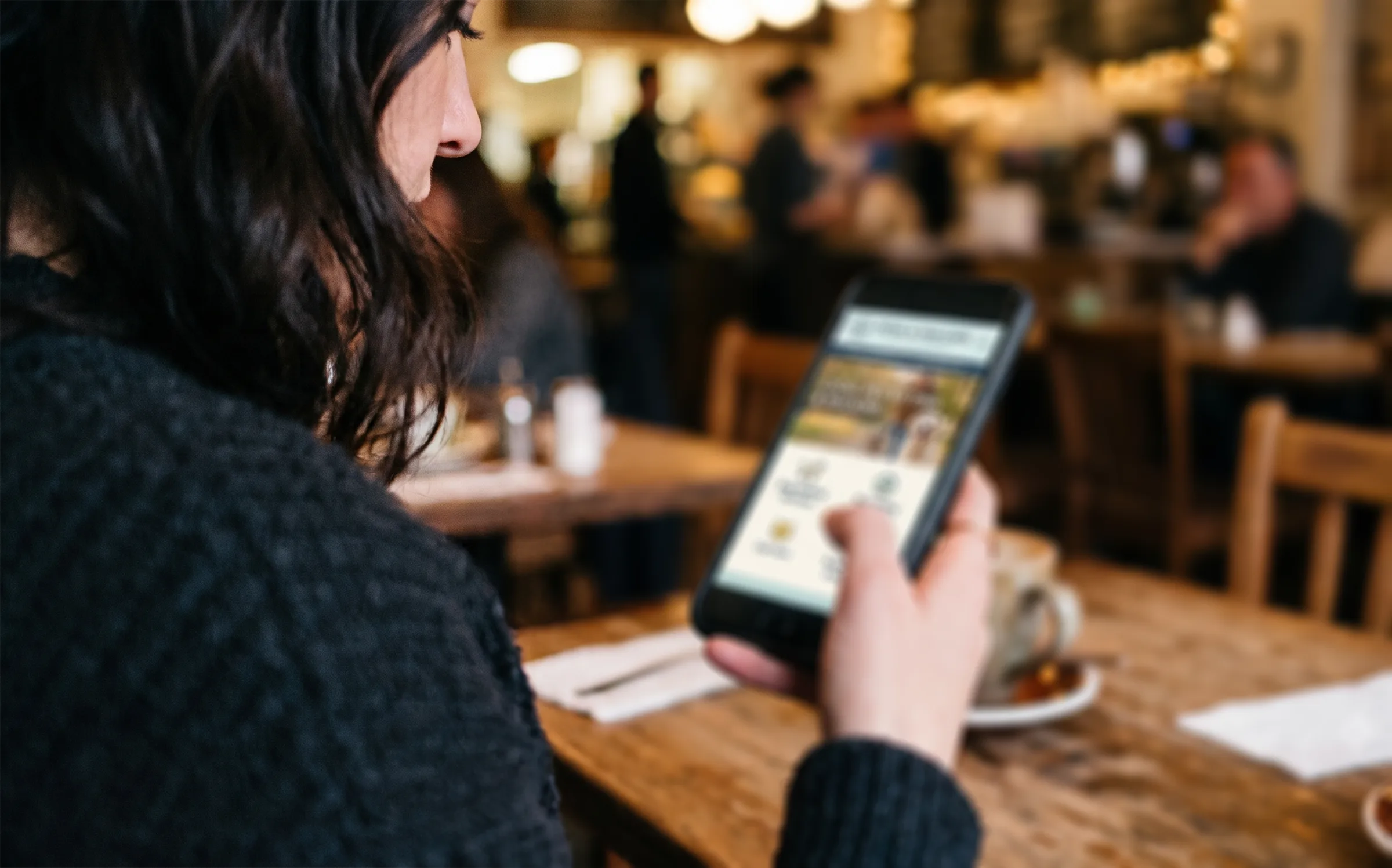 A customer in a café checking a local business’s website on her phone